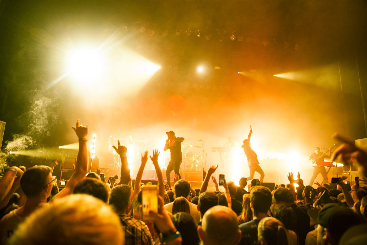Dirty Heads performing live on stage with bright golden lights and an energetic crowd in the foreground.