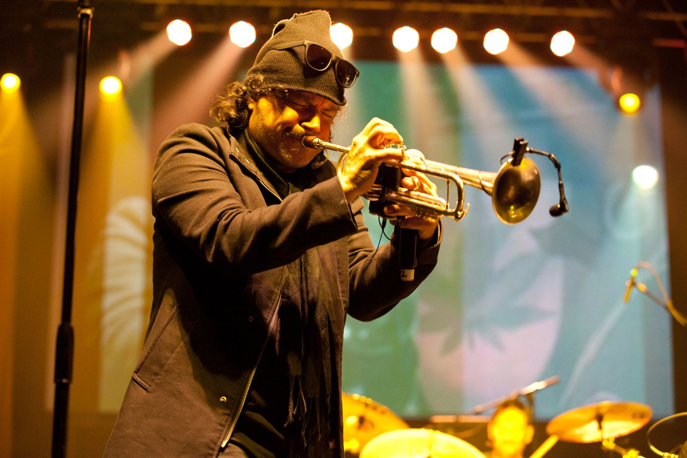 Trumpet player from Ozomatli performing live on stage under warm concert lighting.