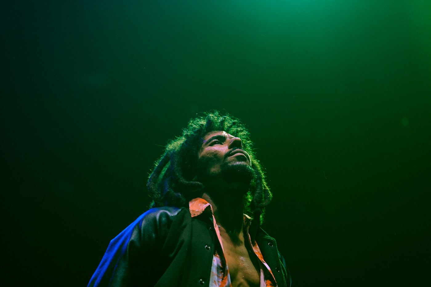 Reggae vocalist looking upward during a live performance under green stage lighting.