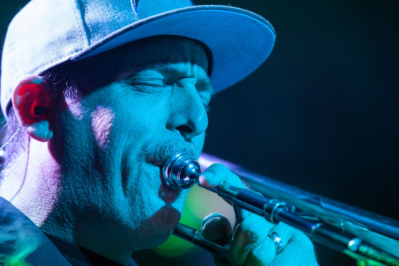 Close-up of a trombone player performing live on stage under blue concert lighting.